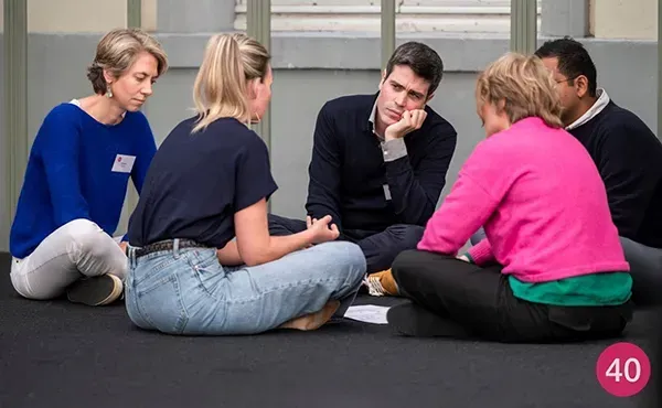 Marie-Paule zittend op de grond in overleg met vier andere personen